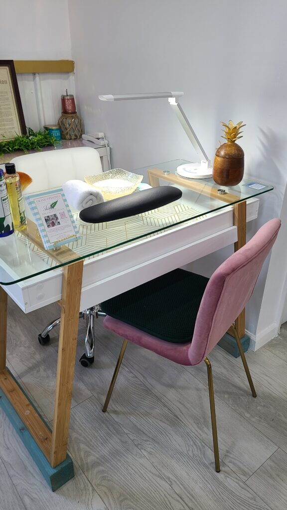 Desk with with glass top and pink chair with a black cushion located at Shades By Shar